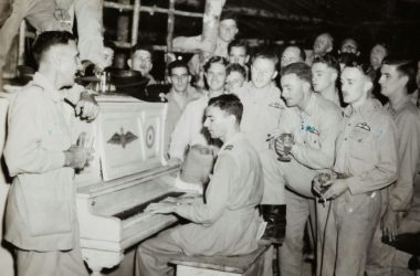 grayscale photo of 4 men standing beside piano