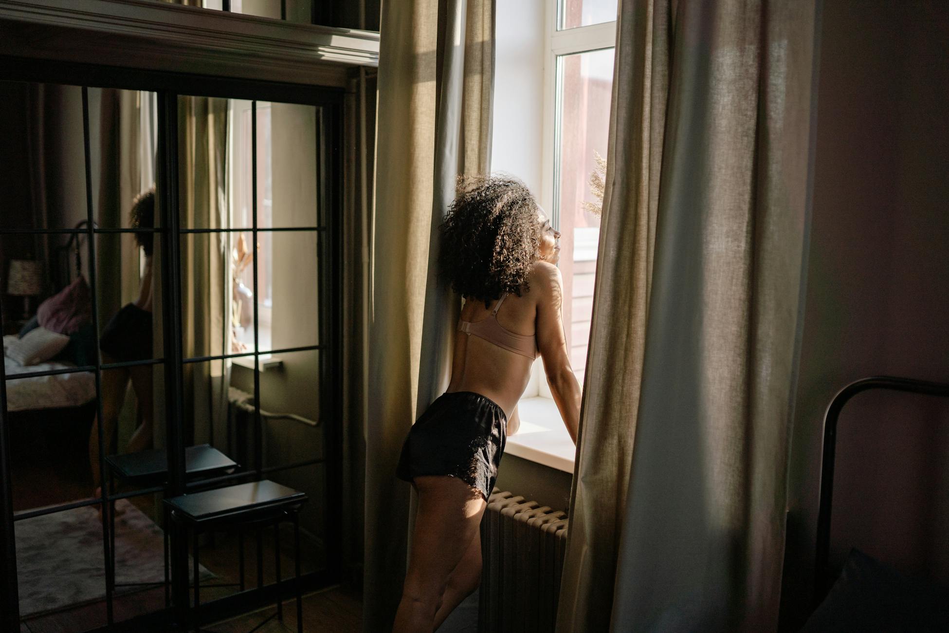 A woman in lingerie gazes through a window in a stylish living room setting.