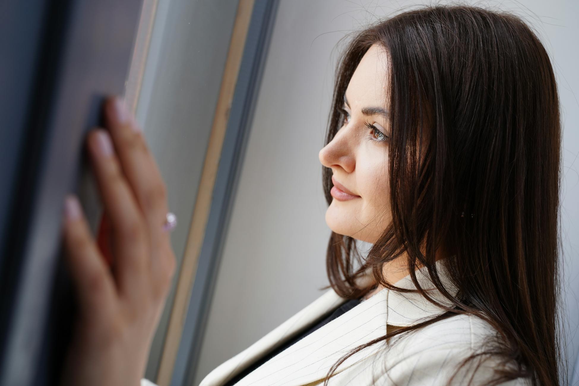 A thoughtful woman in professional attire gazing through a window indoors.