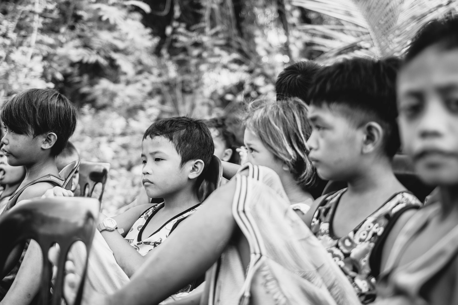 Black and white photo of children seated outside, displaying thoughtful expressions.