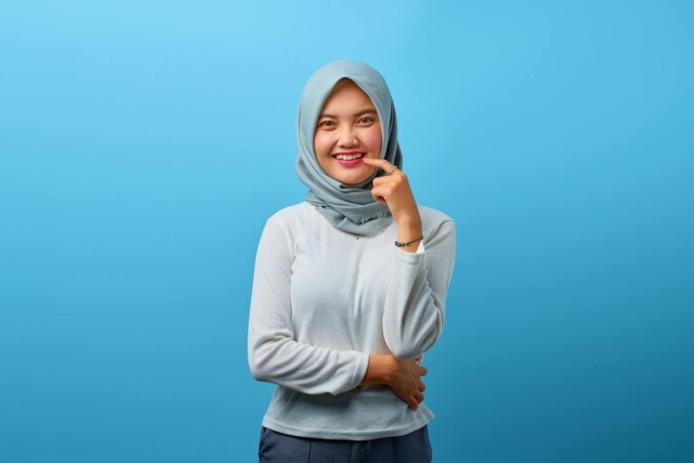 Cheerful teenage girl wearing hijab, posing in front of a bright blue backdrop.