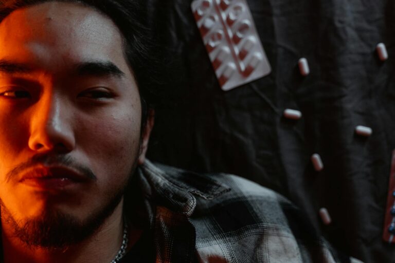 Close-up of a man's face with a dramatic light, surrounded by pills, conveying anxiety.