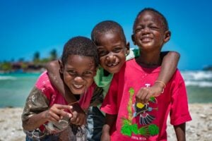 Three happy children embracing on a sunny beach in Honduras, showcasing friendship and joy.