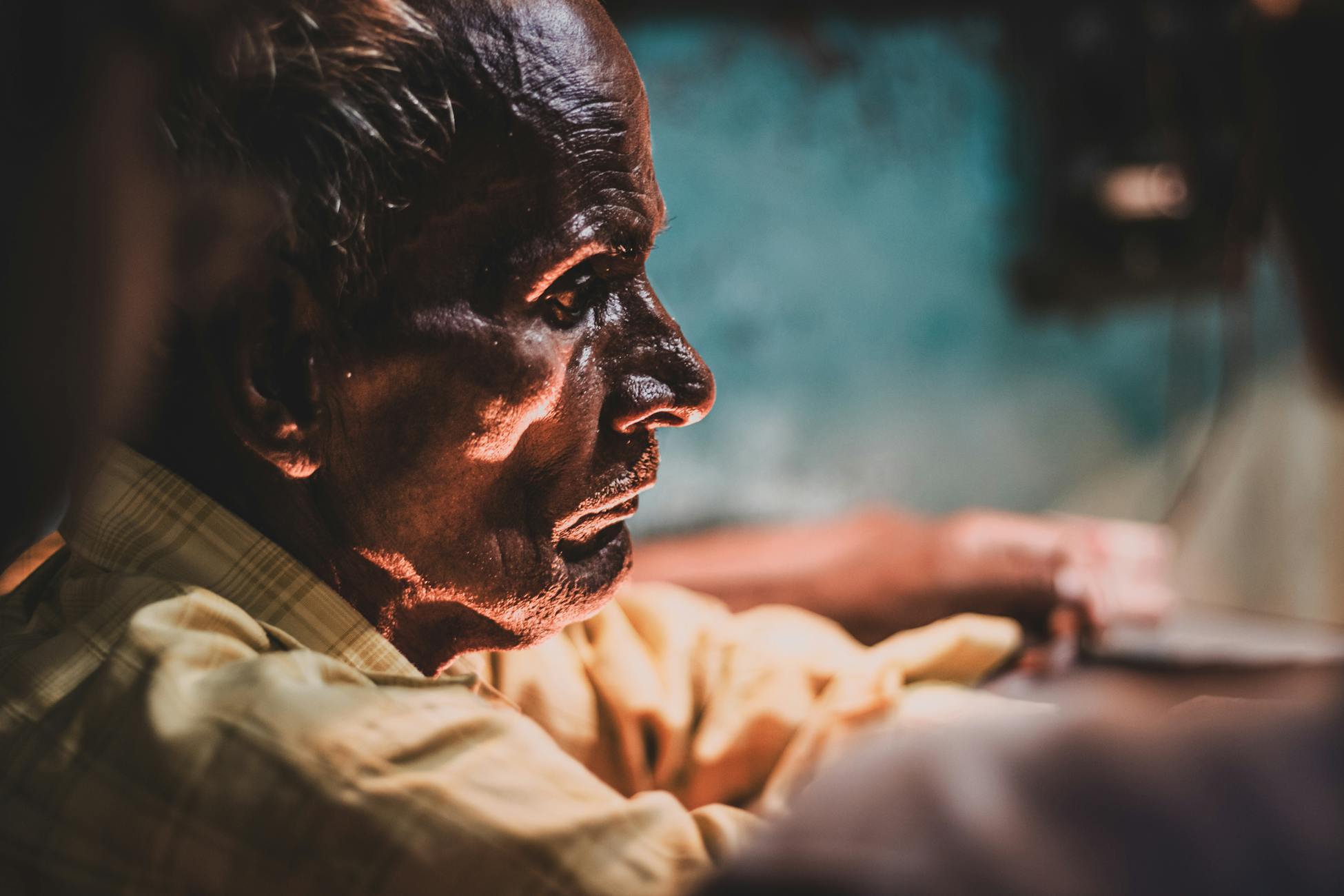 A dramatic side view of an elderly man with deep wrinkles and a focused expression, indoors in Kolkata.