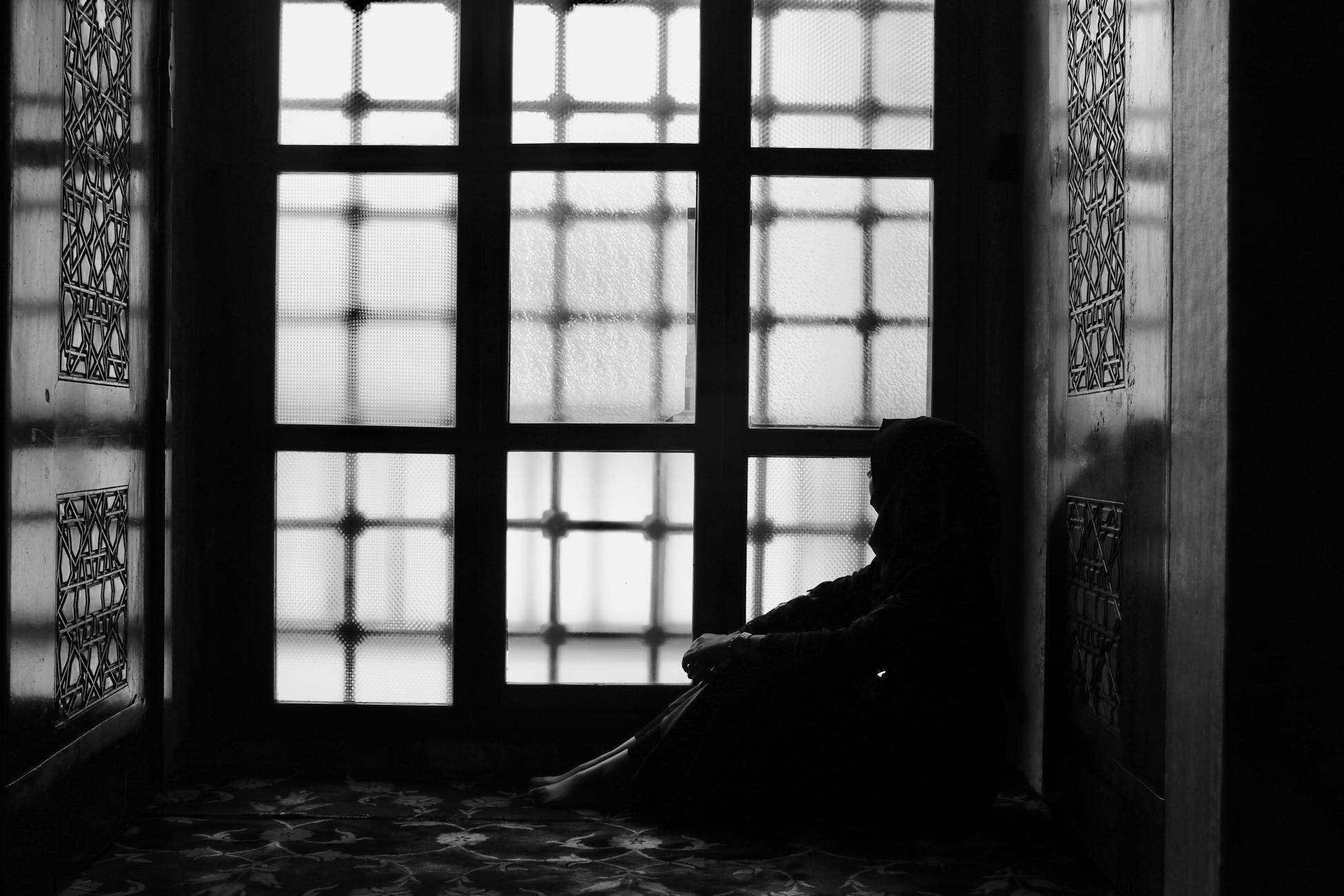 Thoughtful silhouette sitting by an Ottoman-style window in black and white.