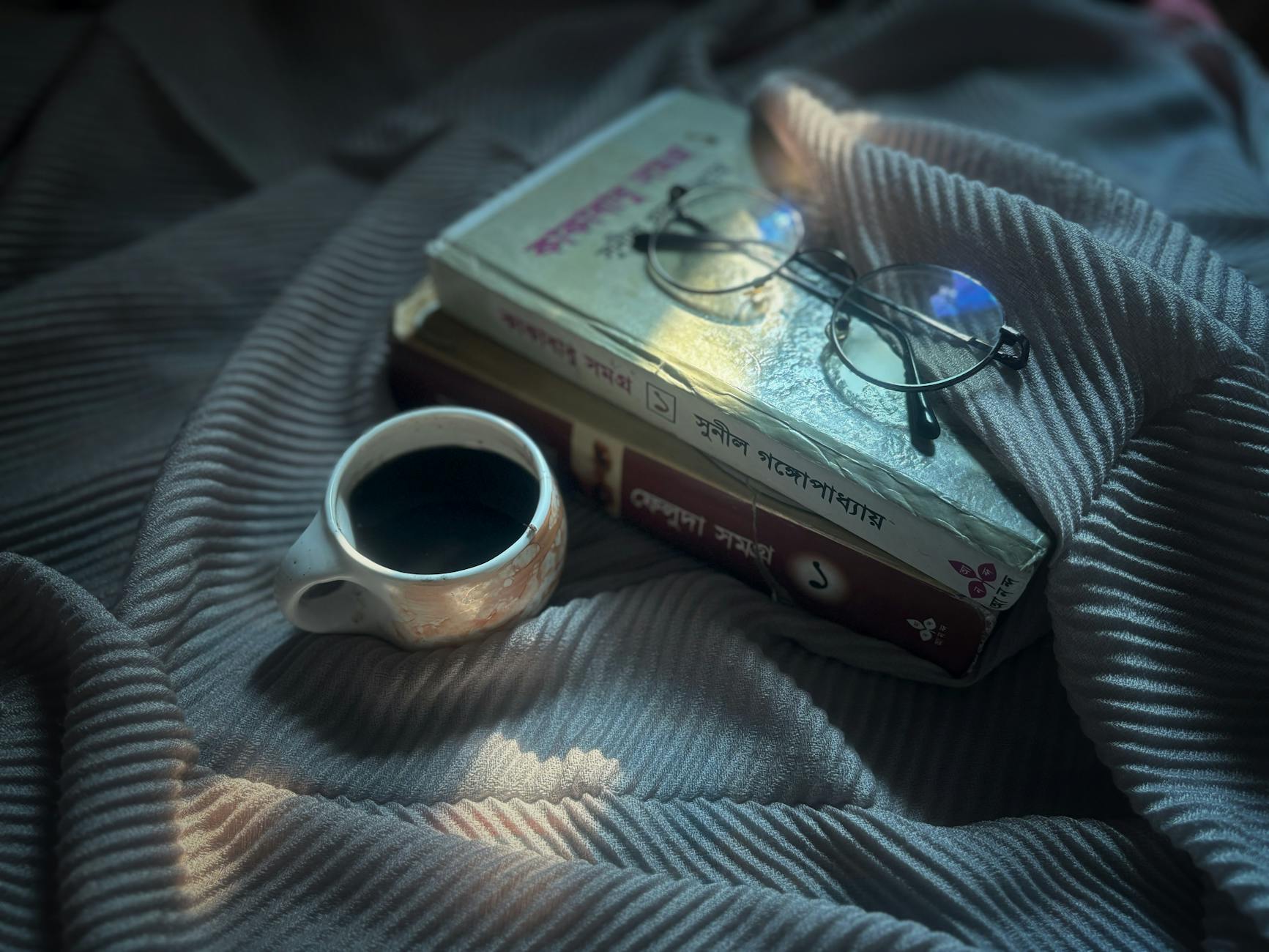 An inviting scene featuring books, glasses, and a cup of coffee on patterned fabric in soft morning light.