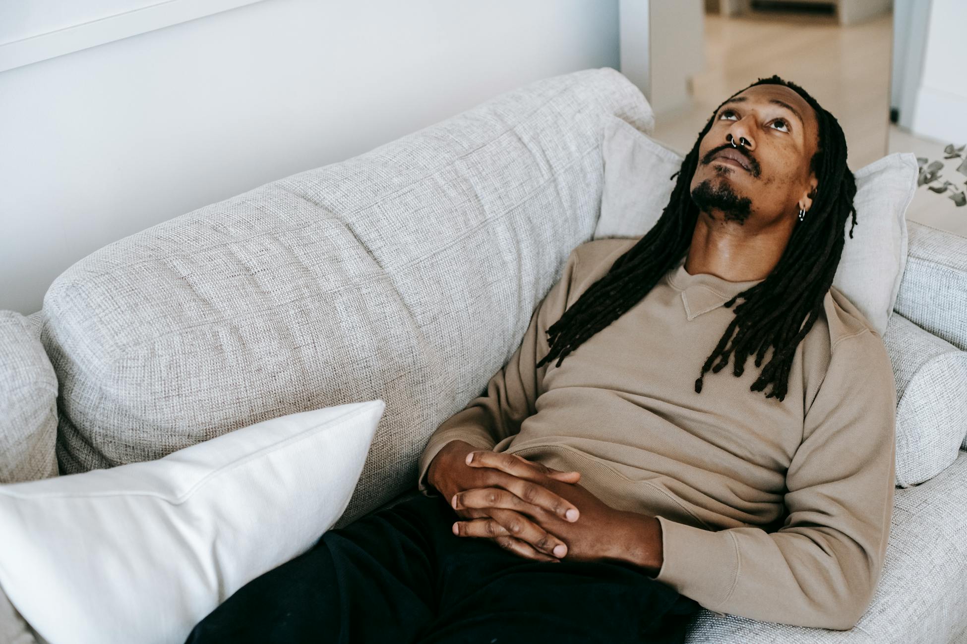 Man with dreadlocks lies on couch, looking up, expressing contemplation and introspection indoors.