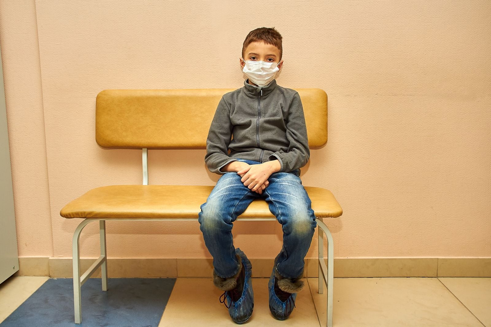 young boy wearing a face mask while sitting on a bench