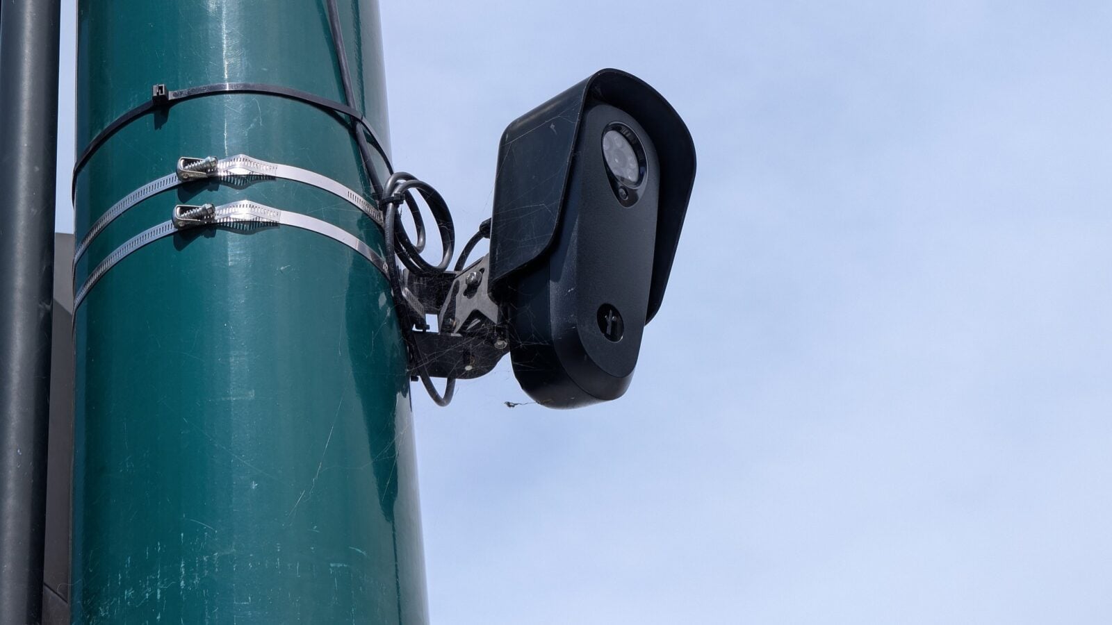 A Flock Safety licence plate camera mounted on a green pole against a blue sky