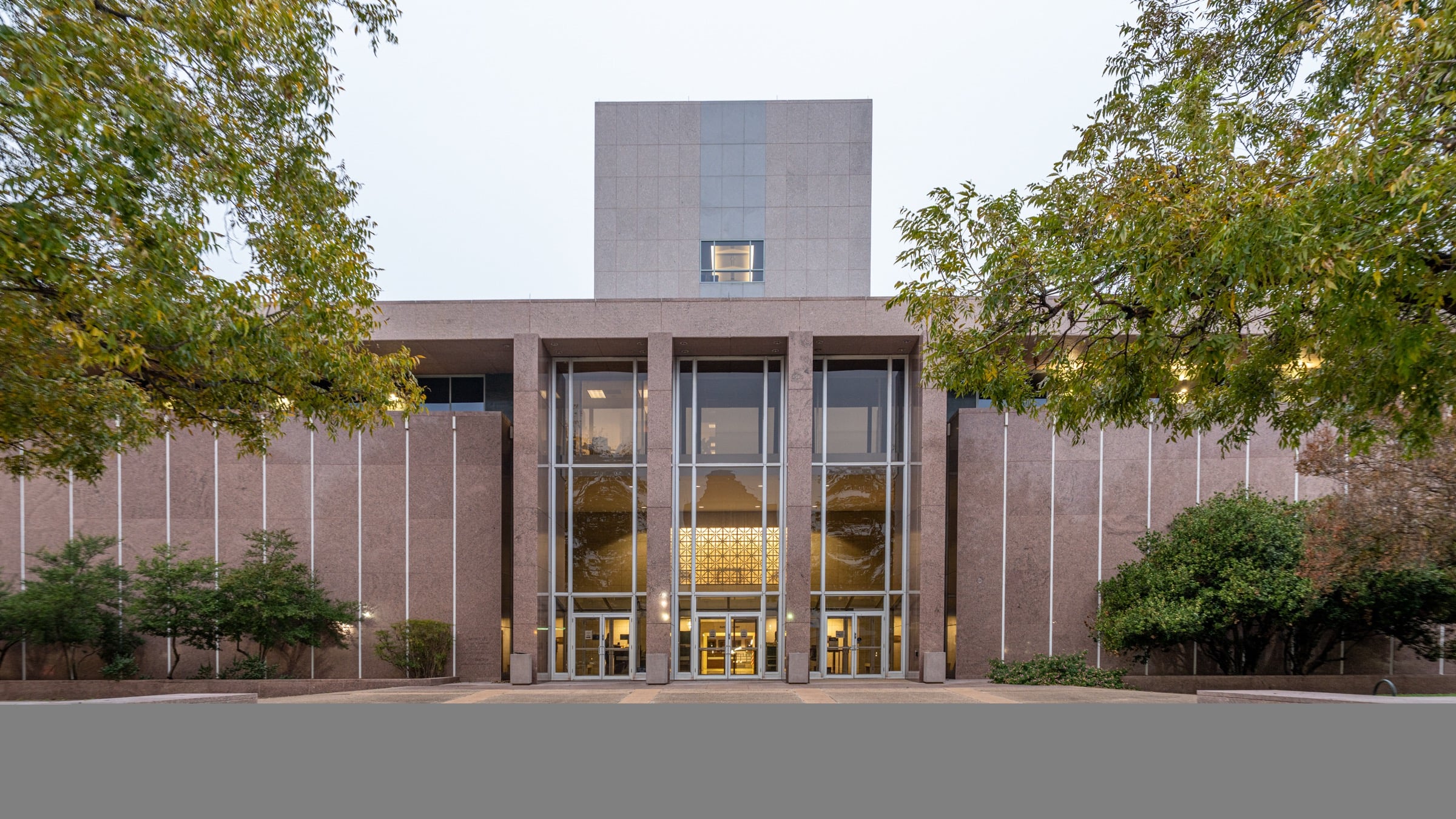 Front of the Supreme Court Building in Austin, a granite building with tall glass windows behind a stone plaza and trees